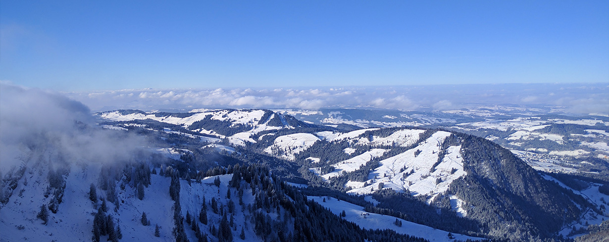„Verschneite Berglandschaft im Allgäu unter blauem Himmel mit weitem Blick bis zum Horizont – Naturidylle im Winter