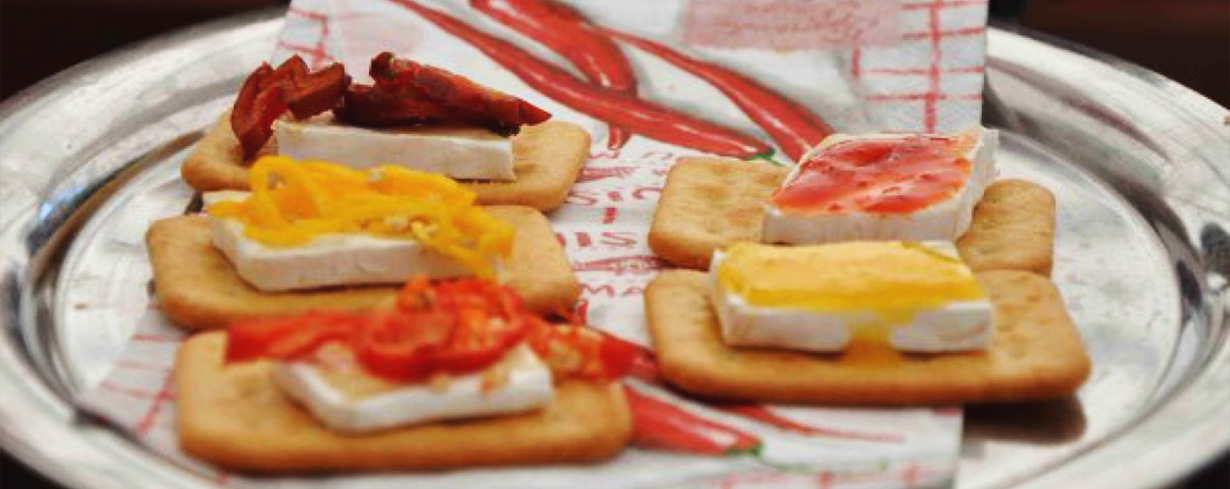 Kräcker mit verschiedenen Toppings aus Käse, Paprika, Tomaten und Marmelade auf einem Serviertablett