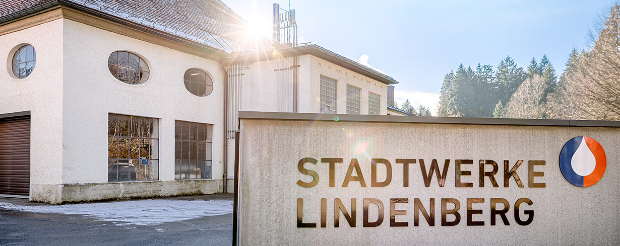 Eingangsbereich der Stadtwerke Lindenberg mit Firmenschild im Vordergrund und historischem Gebäude im Hintergrund bei Sonnenschein